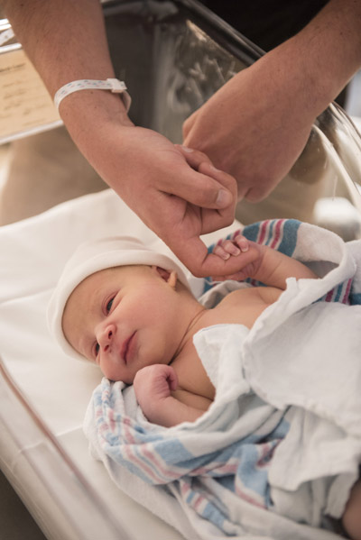 Baby in a crib holding finger of parent